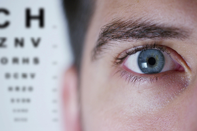 closeup of eye with eye exam chart in background